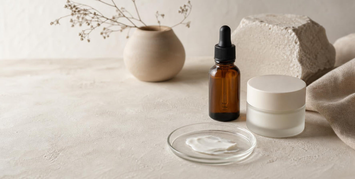 Amber dropper bottle, cream jar and a cream swatch on a glass dish, showing a custom skincare formula in development